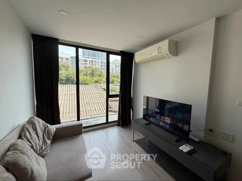 Modern living room with large window and city view, featuring a comfortable sofa and flat-screen TV.