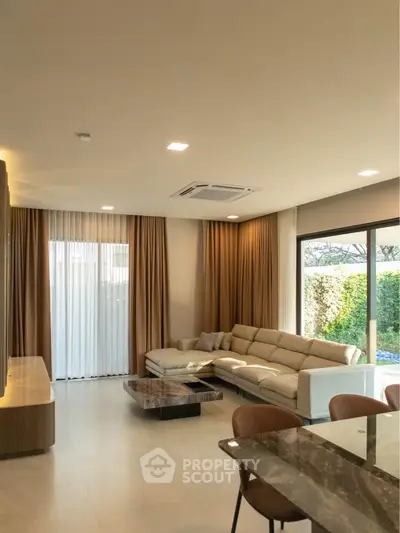 Spacious modern living room with elegant furniture and large windows overlooking a lush garden.