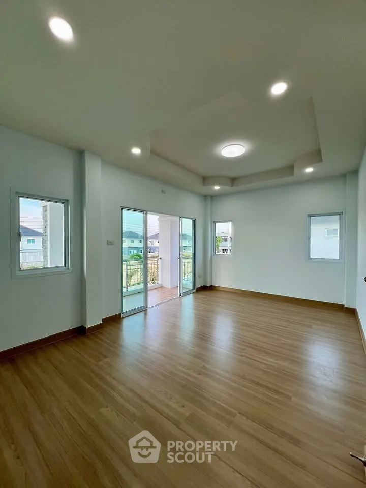 Spacious living room with wooden flooring and large windows offering natural light.