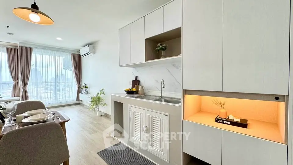 Modern living room with open kitchen and elegant decor, featuring large windows and stylish furnishings.