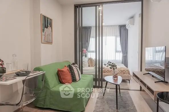 Modern living room with green sofa and glass partition leading to cozy bedroom.