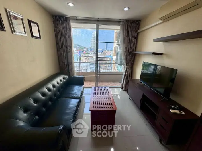 Cozy living room with leather sofa, TV, and balcony view in modern apartment.