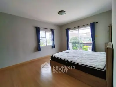 Spacious bedroom with large windows and wooden flooring, offering ample natural light.