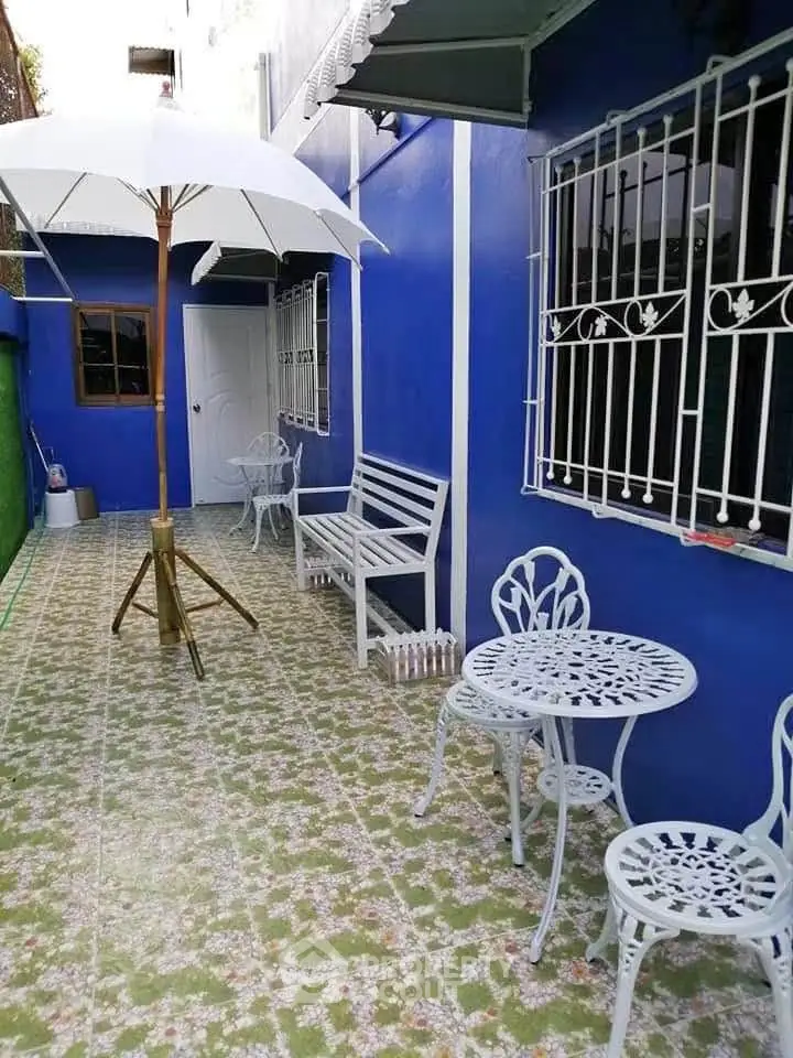 Charming outdoor patio with blue walls, white furniture, and umbrella, perfect for relaxation and entertaining.