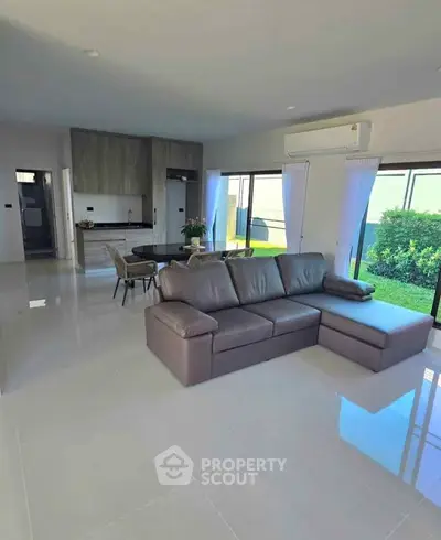 Spacious modern living room with open kitchen and garden view, featuring sleek furniture and abundant natural light.