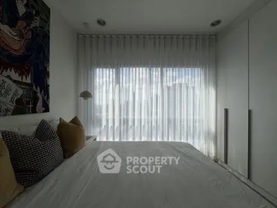 Modern bedroom with large window and sheer curtains offering city view.