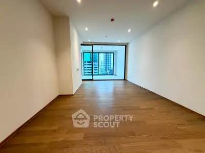 Spacious modern living room with wooden flooring and large windows offering city views.