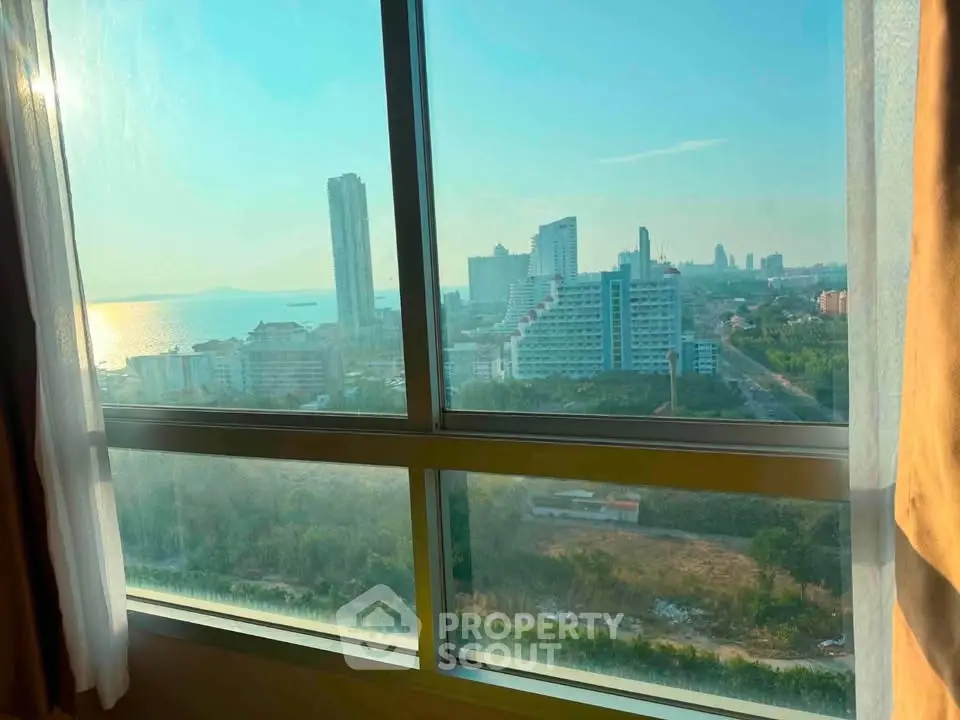 Stunning high-rise view from a window overlooking a vibrant cityscape and ocean horizon.