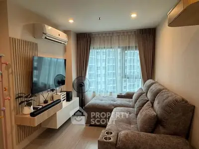 Cozy living room with plush sofa, wall-mounted TV, and large window view in modern apartment.