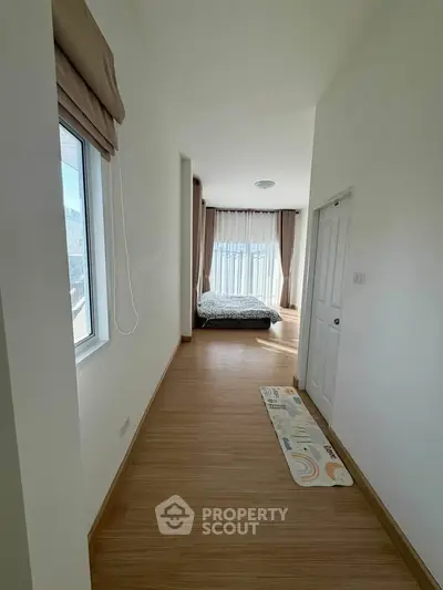 Bright hallway leading to a cozy bedroom with large windows and wooden flooring.