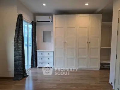 Spacious bedroom with wooden flooring, large wardrobe, and natural light from balcony.