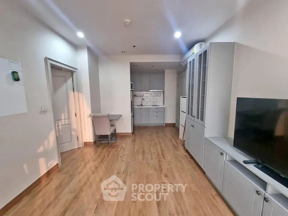 Modern open-plan living room with wooden flooring and sleek kitchen cabinetry.