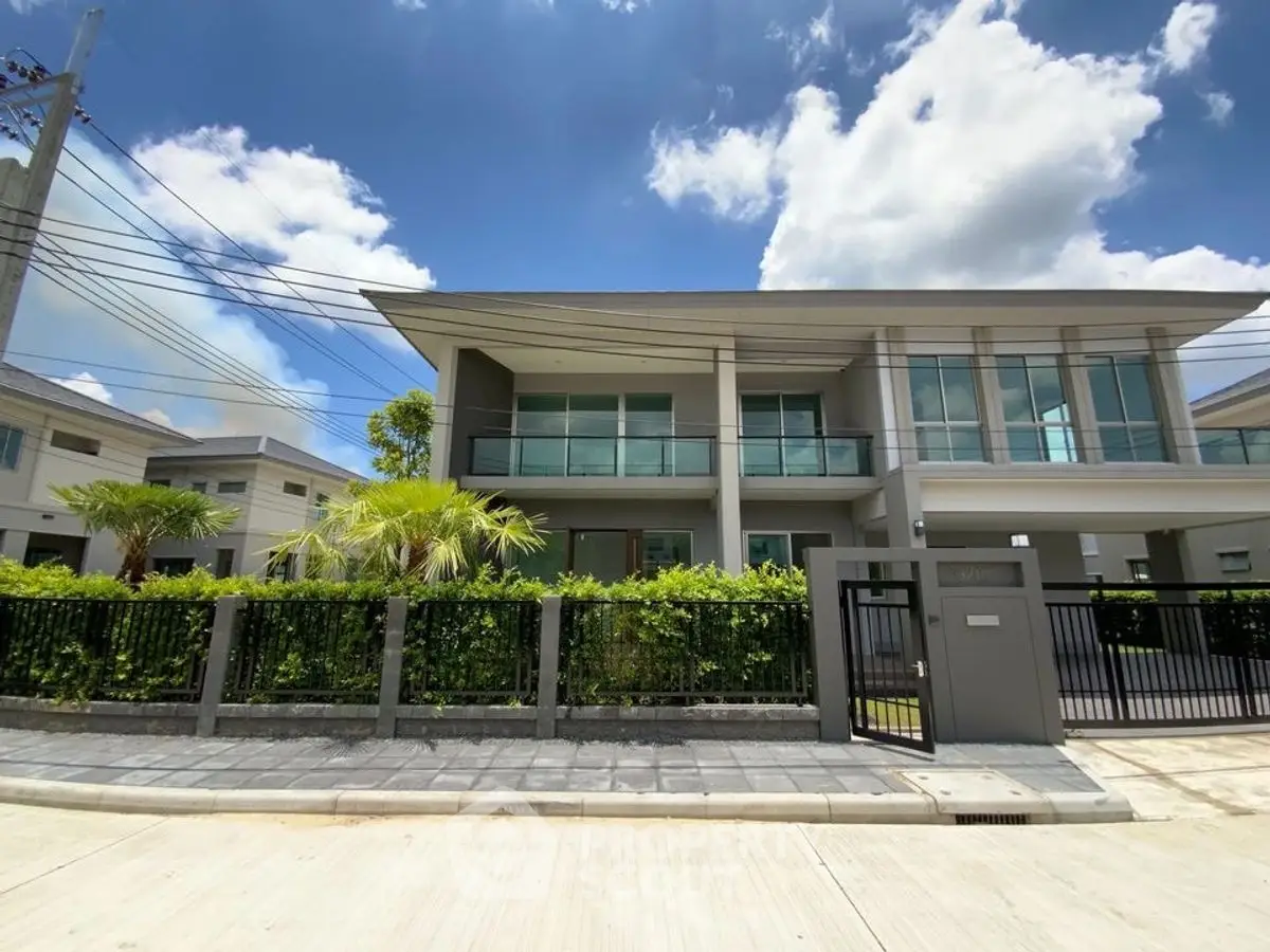 Modern two-story house with large windows and lush greenery under a bright blue sky.