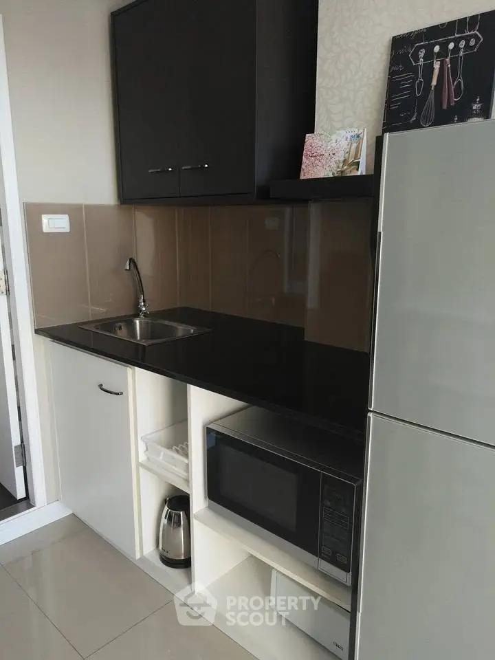 Modern kitchen with sleek black countertop, microwave, and fridge in compact layout.