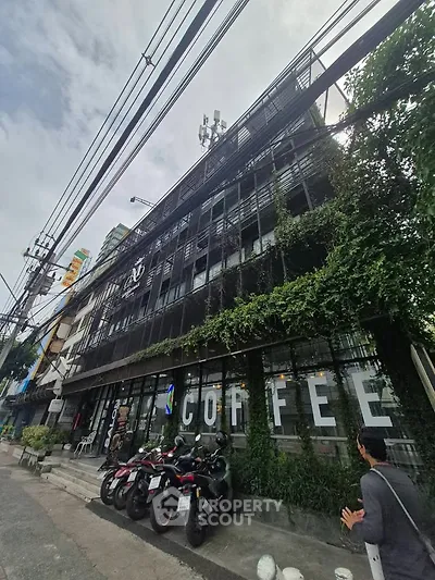 Chic urban building with lush greenery and street view, perfect for a trendy coffee shop location.