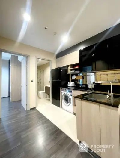 Modern kitchen with sleek black appliances, wooden cabinetry, and integrated laundry area, featuring a bright, open layout perfect for urban living.