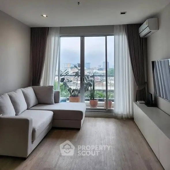 Modern living room with large window and city view, featuring a cozy sofa and sleek TV setup.