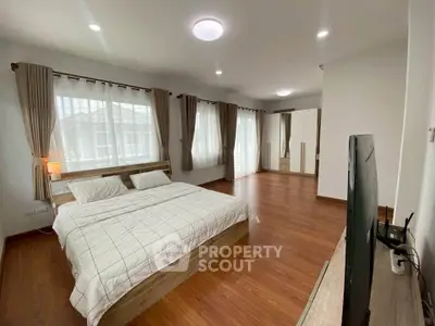Spacious modern bedroom with wooden flooring and large windows for natural light.