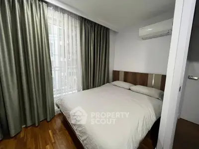 Cozy bedroom with wooden flooring and air conditioning, featuring a large window with elegant curtains.