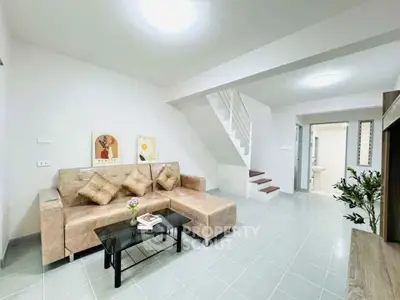 Modern living room with beige sofa and sleek staircase in bright, airy space.