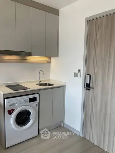 Modern compact kitchen with washing machine and sleek cabinetry in a stylish apartment.