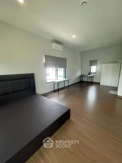 Spacious modern bedroom with wooden flooring and large windows for natural light.