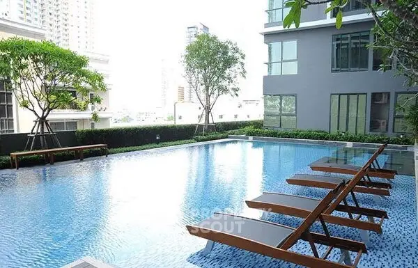 Luxurious condominium pool area with modern lounge chairs and lush greenery.