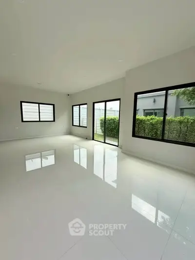 Spacious modern living room with large windows and glossy white tiles, offering abundant natural light.