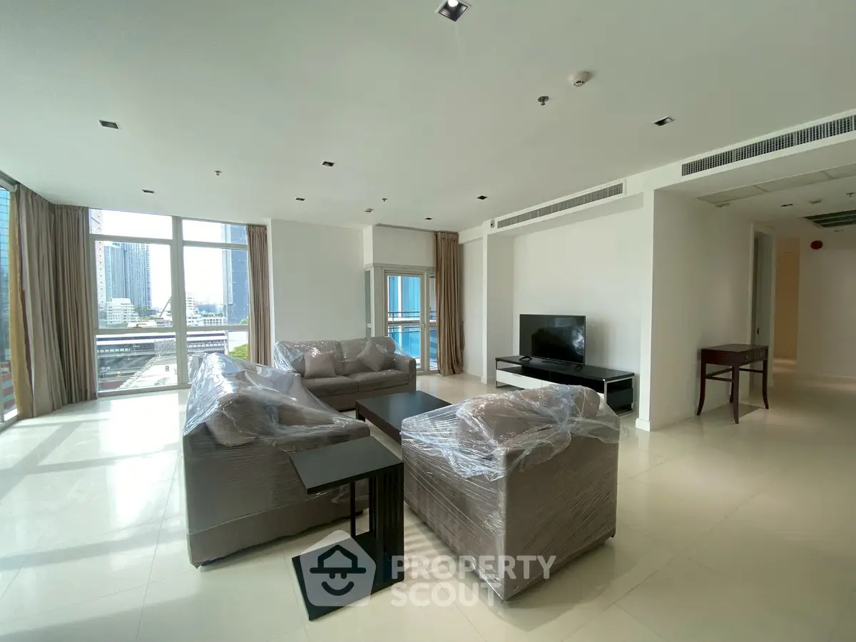 Spacious modern living room with large windows and city view, featuring comfortable seating and sleek decor.