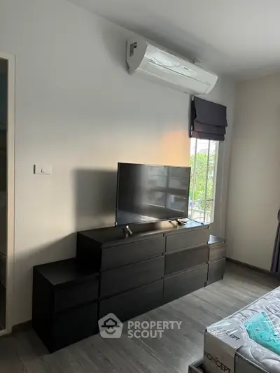 Modern bedroom with sleek black dresser and mounted TV, featuring air conditioning and natural light.