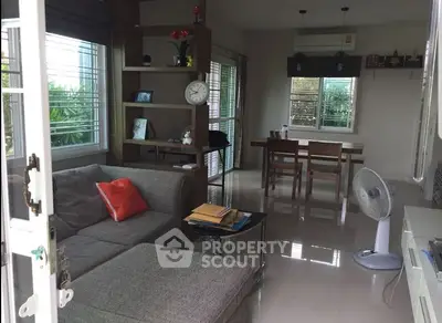 Modern living room with cozy gray sofa and dining area, featuring large windows and natural light.