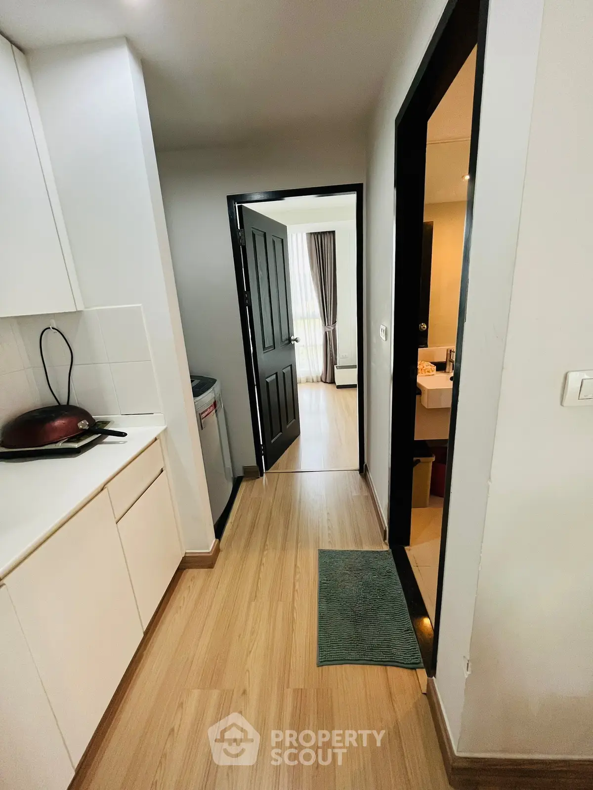 Modern apartment hallway with wooden flooring and sleek kitchen cabinets.
