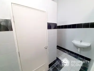 Compact bathroom with white and navy blue tiles, featuring a small wall-mounted sink and a mirrored medicine cabinet.