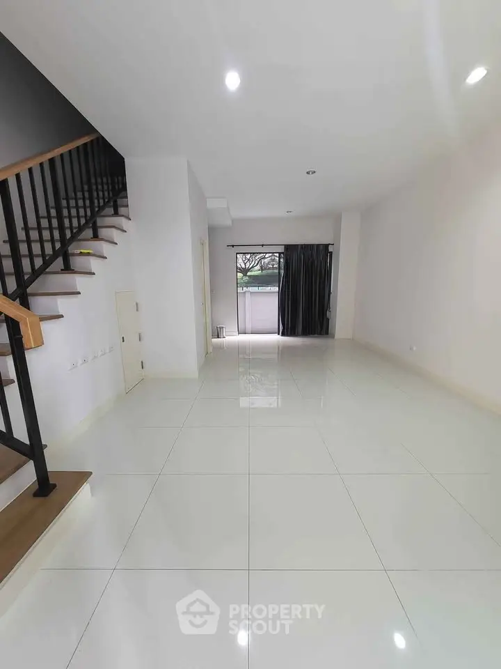 Spacious modern living room with sleek staircase and large windows for natural light.