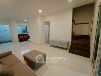 Spacious modern living room with sleek furniture and staircase, perfect for family gatherings.