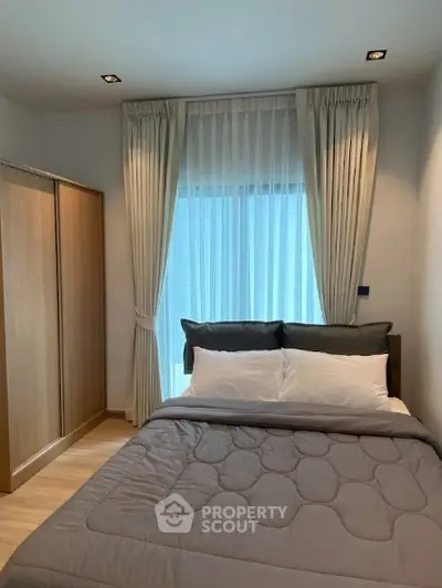 Cozy bedroom with modern decor and ample natural light from large window.