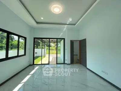 Spacious living room with large windows and garden view, featuring modern ceiling light and glossy floor tiles.