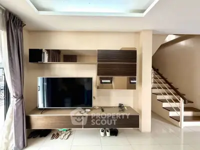 Modern living room with sleek TV unit and staircase, showcasing contemporary interior design.