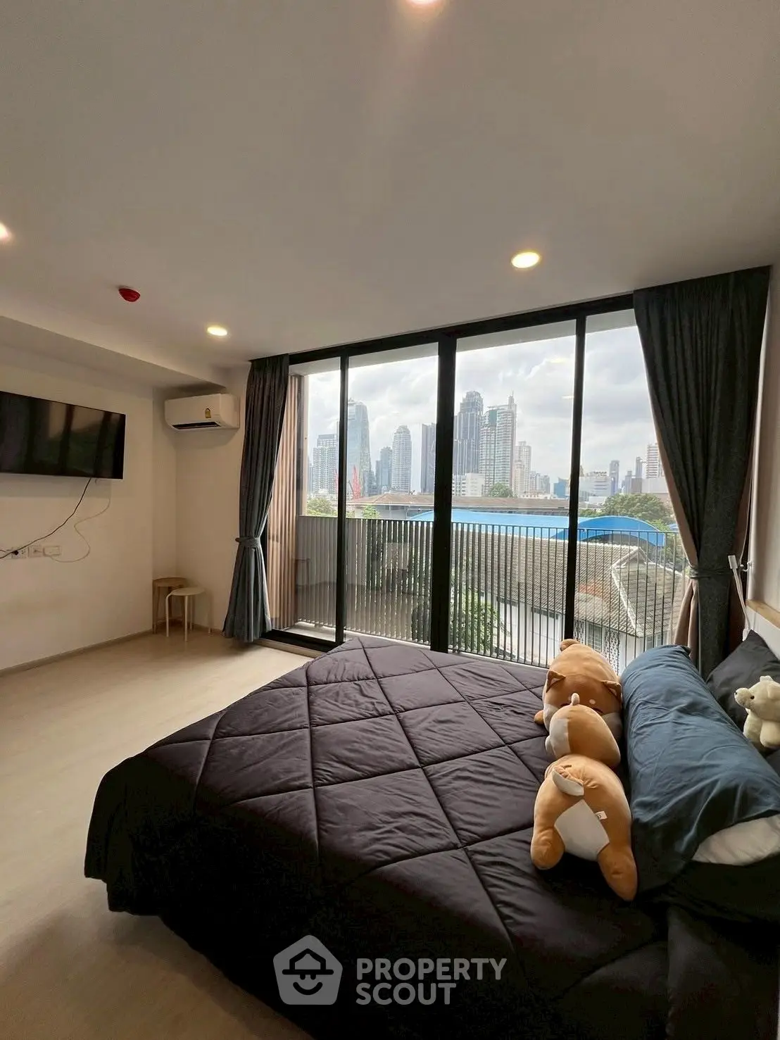Spacious bedroom with city view and large windows in modern apartment.