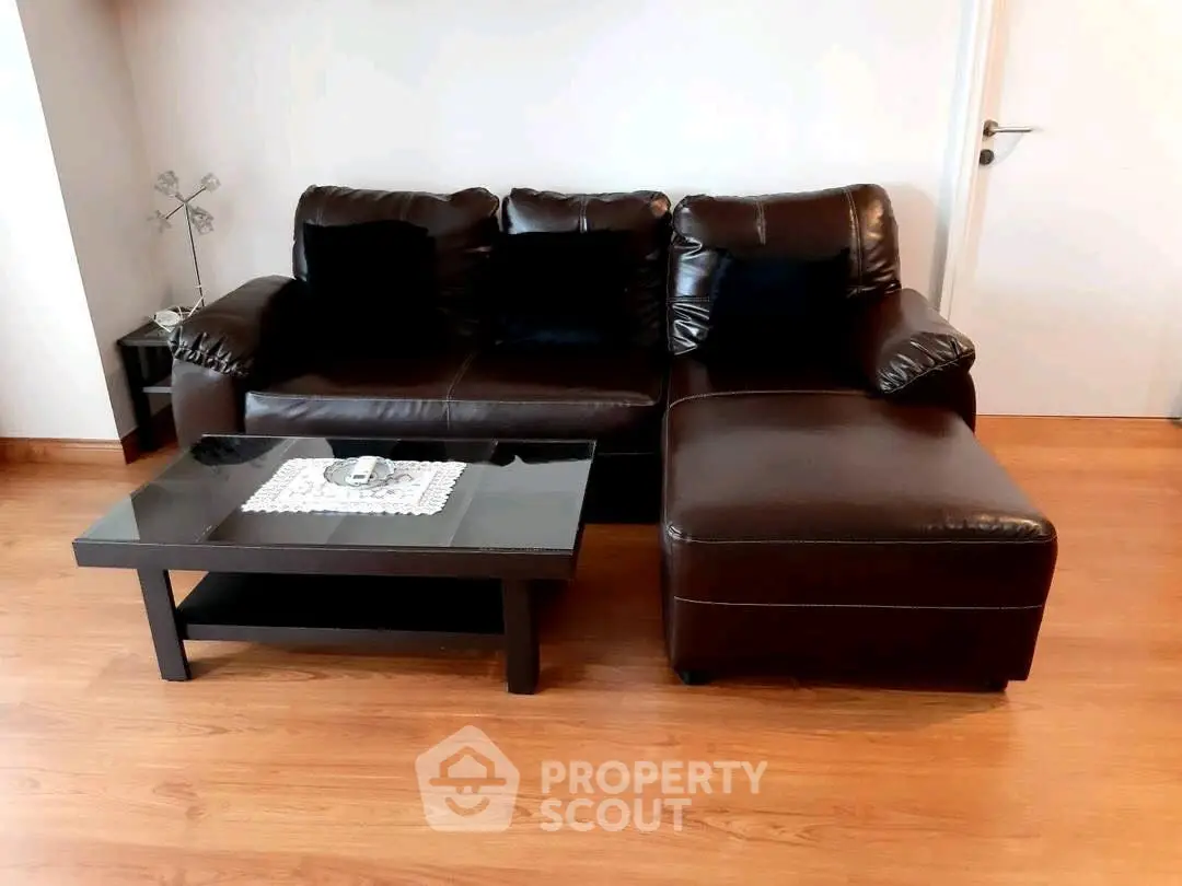 Stylish living room with dark leather sofa and modern glass coffee table on wooden flooring.