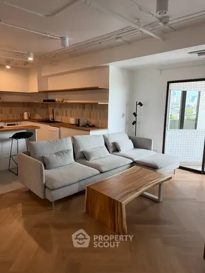Modern living room with open kitchen and stylish wooden flooring, featuring a cozy sofa and sleek coffee table.