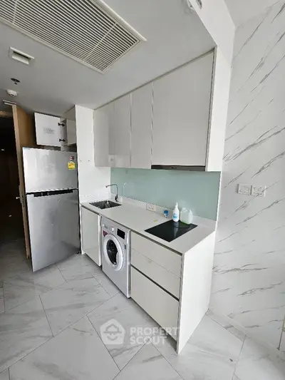 Modern kitchen with sleek cabinetry, integrated washing machine, and compact fridge in a stylish apartment.