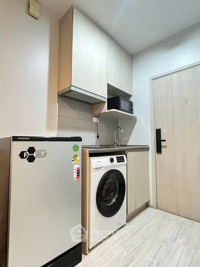 Compact kitchen with modern appliances including washing machine and fridge, light wood cabinets, and sleek design.