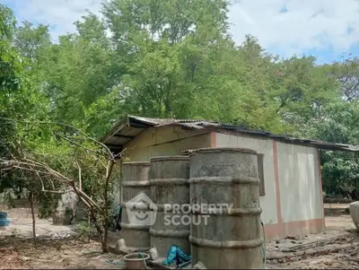 Rustic rural property with metal roof and large water storage tanks surrounded by lush greenery.