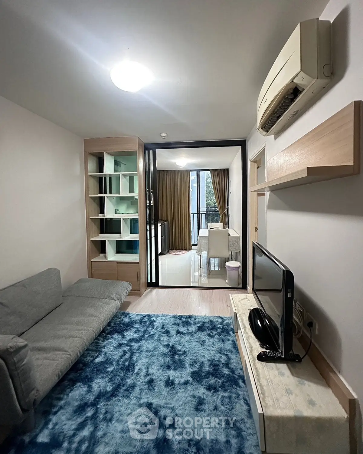 Modern living room with cozy sofa, blue rug, and air conditioning, leading to a bright dining area with balcony view.