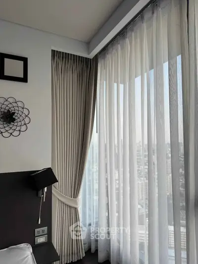 Luxurious bedroom with floor-to-ceiling windows offering stunning city views and elegant decor.