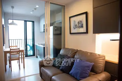 Modern living room with cozy sofa and open kitchen leading to a balcony with natural light.