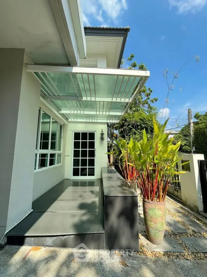 Charming modern home entrance with glass awning and lush greenery