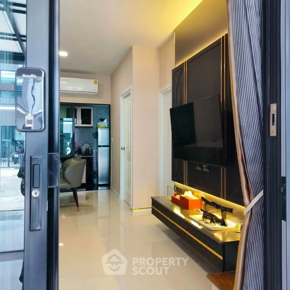 Modern living room with sleek TV setup and view into stylish kitchen area.