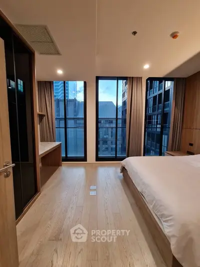 Modern bedroom with large windows offering city views in a high-rise apartment.
